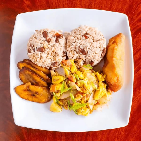 A Jamaican breakfast plate with ackee and saltfish, rice and peas, fried plantains, and a fried dumpling.