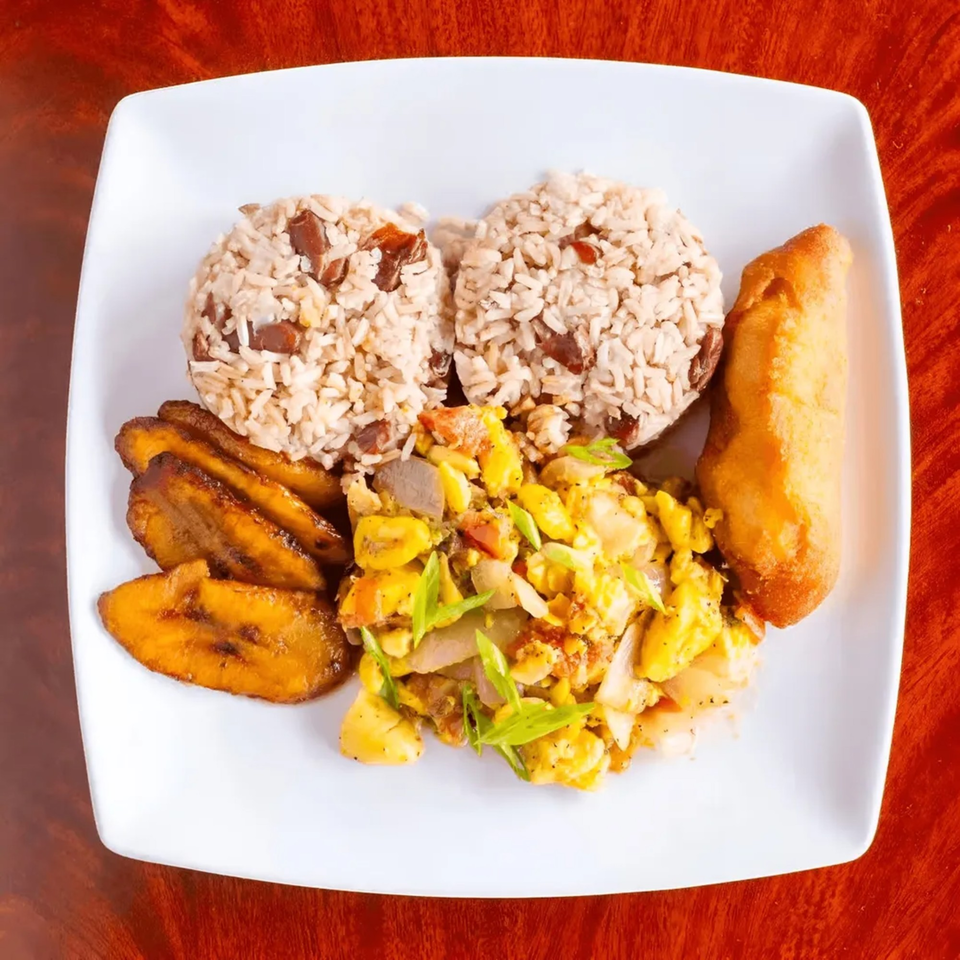 A Jamaican breakfast plate with ackee and saltfish, rice and peas, fried plantains, and a fried dumpling.