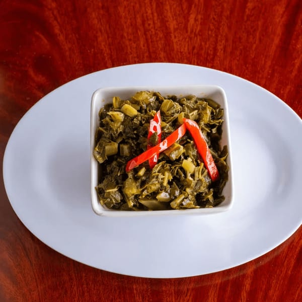 A white square bowl of callaloo, a Jamaican vegetable dish, garnished with red chili peppers.
