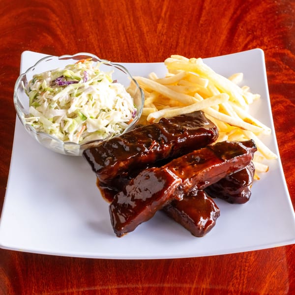 Flavas Jamaican Grill ribs with barbecue sauce, french fries, and coleslaw on a white plate.